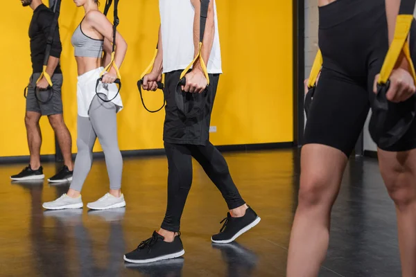 Vista recortada del deportista tirando de correas de suspensión cerca de amigos en el gimnasio - foto de stock