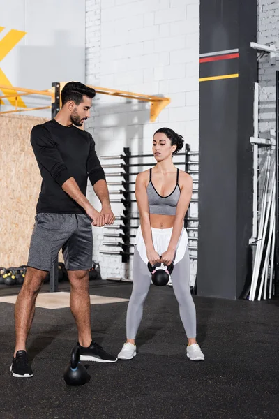 Arabian trainer standing near middle east sportswoman training with kettlebell in gym — Stock Photo