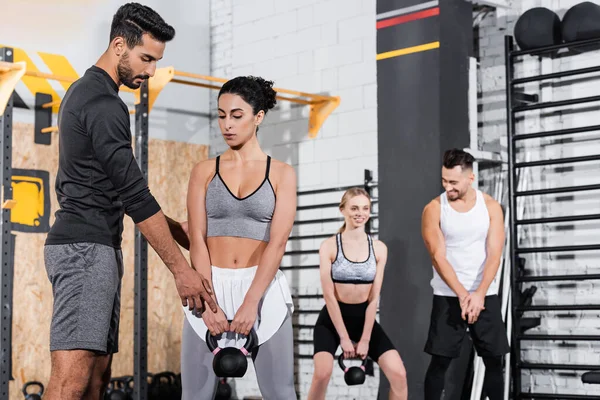 Muslim trainer pointing at kettlebell near middle east sportswoman in gym — Stock Photo