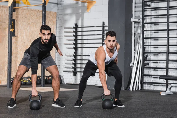 Multiethnic sportsmen training with kettlebells in gym — Stock Photo