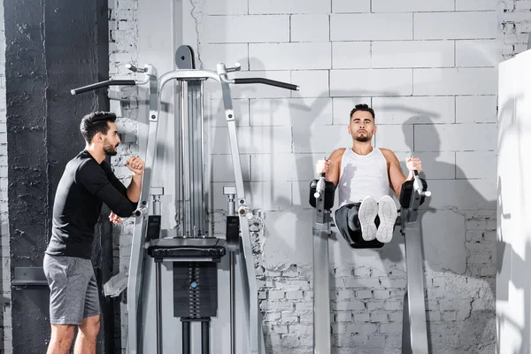 Sportlertraining am Parallelbarren neben arabischem Trainer im Fitnessstudio — Stockfoto