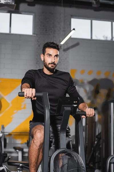 Muslim sportsman training on elliptical trainer in blurred gym — Stock Photo