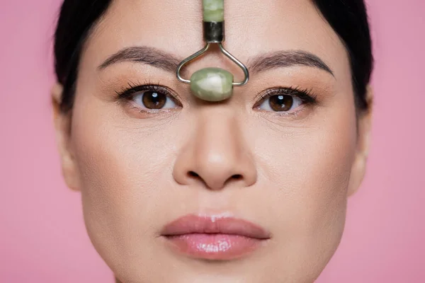 Close up view of jade roller near nose of asian woman isolated on pink — Stock Photo