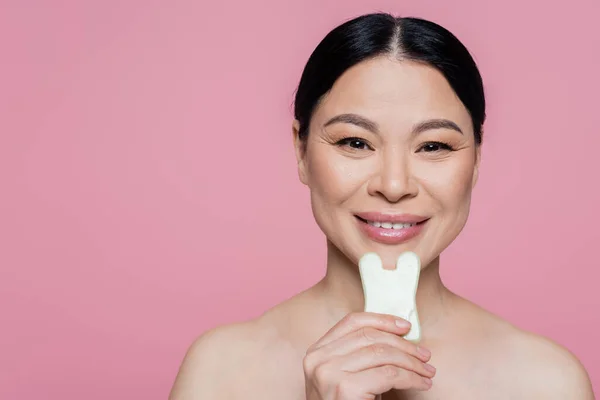 Smiling asian woman with naked shoulders holding jade stone isolated on pink — Stock Photo