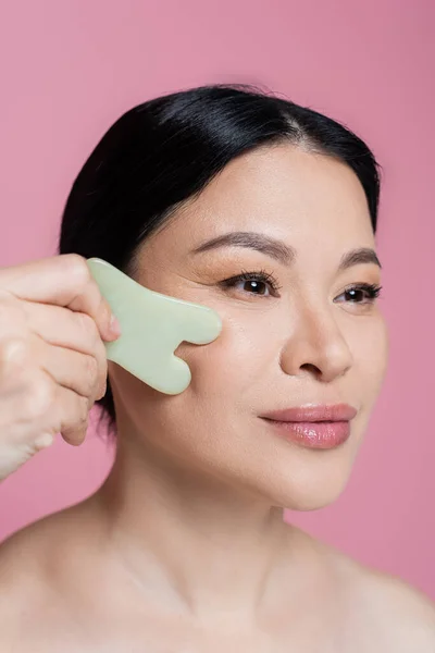 Asian woman massaging cheek with jade stone isolated on pink — Stock Photo