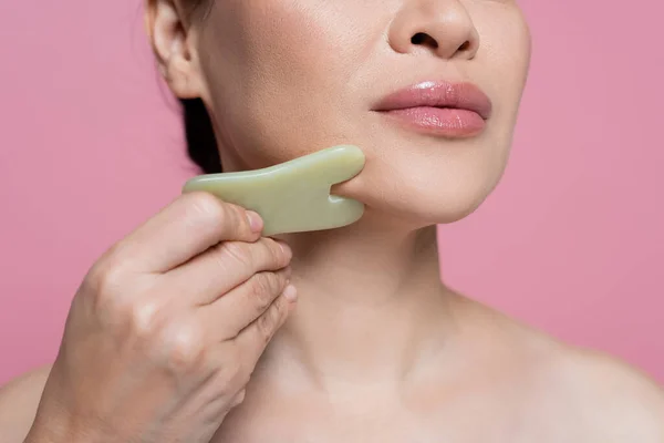 Cropped view of woman with naked shoulder massaging chin with jade stone isolated on pink — Stock Photo