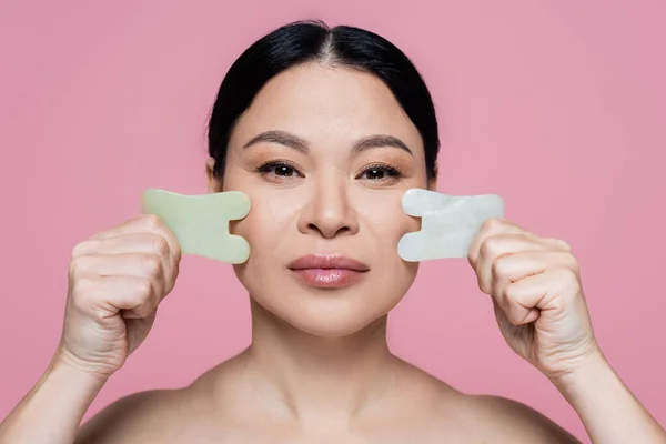 Mujer asiática sosteniendo piedras de jade cerca de mejillas aisladas en rosa - foto de stock