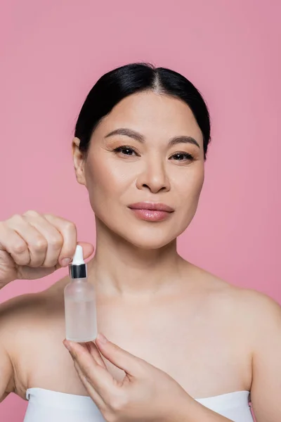 Asian woman in top holding serum isolated on pink — Stock Photo