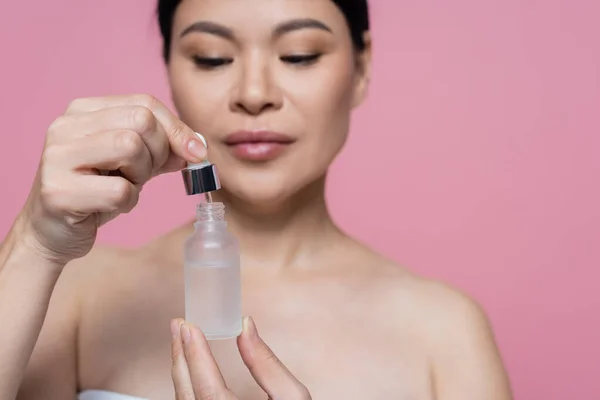 Bottle of serum in hands of blurred asian woman isolated on pink — Stock Photo