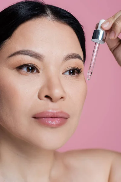 Vista de cerca de la mujer asiática aplicando suero en la cara aislado en rosa - foto de stock