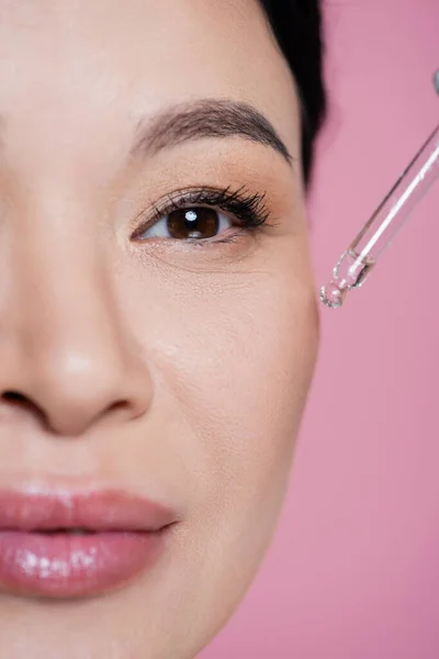 Cropped view of asian woman applying serum on cheek isolated on pink — Stock Photo