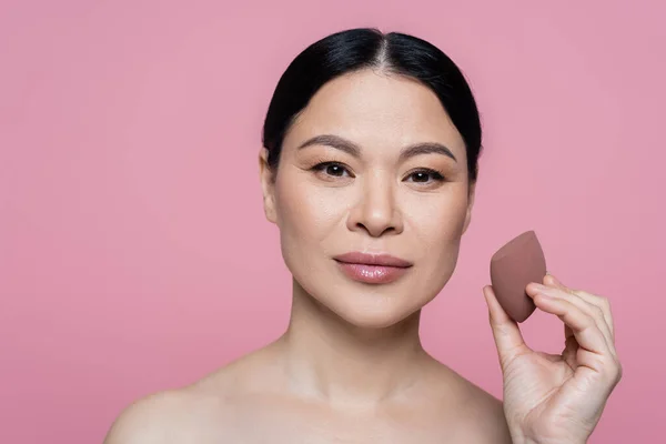 Asian woman with naked shoulders holding beauty blender isolated on pink — Stock Photo