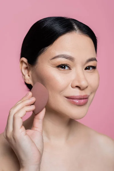 Sourire asiatique femme application visage fond de teint avec beauté mélangeur isolé sur rose — Photo de stock