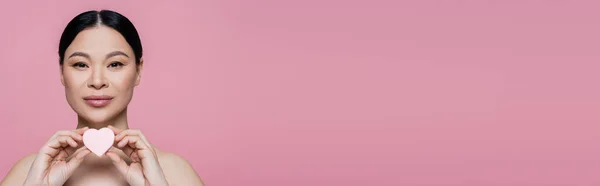 Mulher asiática com ombros nus segurando coração em forma de liquidificador de beleza isolado em rosa, banner — Fotografia de Stock
