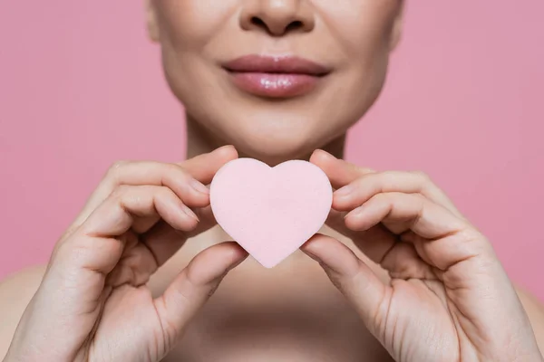 Cropped view of blurred woman holding heart shaped beauty blender isolated on pink — Stock Photo