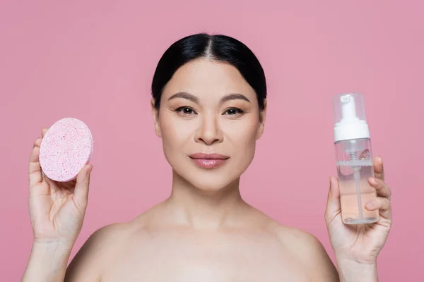 Femme asiatique avec des épaules nues tenant éponge et mousse nettoyante isolée sur rose — Photo de stock