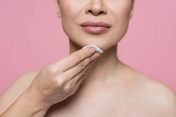 Cropped view of woman with naked shoulders cleaning chin with cotton pad isolated on pink — Stock Photo