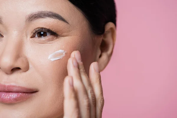 Vista ritagliata della donna asiatica che applica la crema sul viso isolato sul rosa — Foto stock