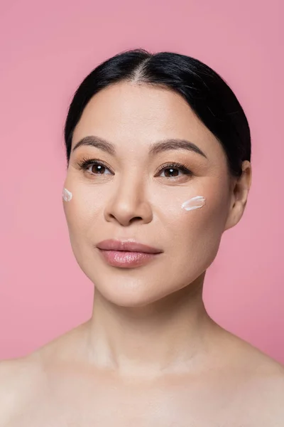 Asiatische Frau mit nackten Schultern und Creme im Gesicht isoliert auf rosa — Stockfoto