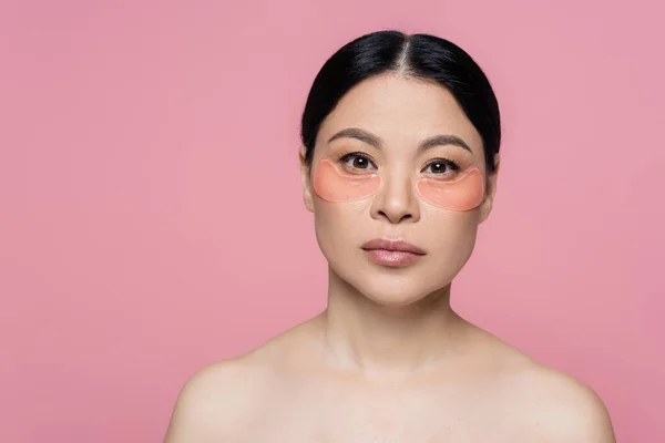 Femme asiatique avec des épaules nues et des patchs pour les yeux regardant la caméra isolée sur rose — Photo de stock