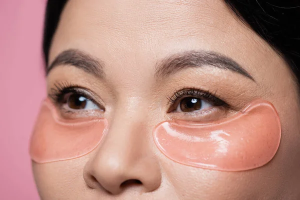 Vista recortada de mujer asiática con parches en los ojos mirando hacia otro lado aislado en rosa - foto de stock