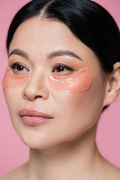 Портрет азиатской женщины с повязками на глазу, смотрящей в сторону изолированной на розовый — стоковое фото