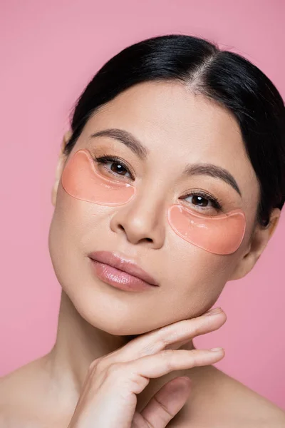 Retrato de mujer asiática con parches en los ojos mirando a la cámara aislada en rosa - foto de stock