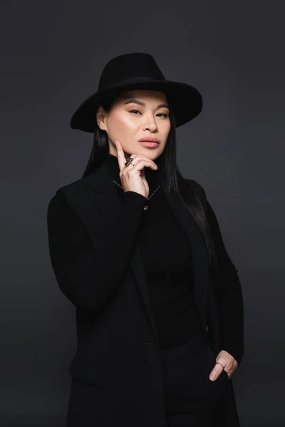 Elegante modelo asiático en sombrero fedora posando aislado sobre gris oscuro - foto de stock