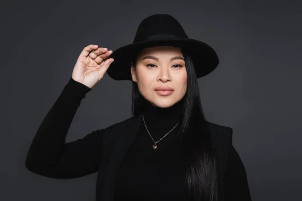 Retrato de mujer asiática tocando sombrero fedora aislado en gris oscuro - foto de stock