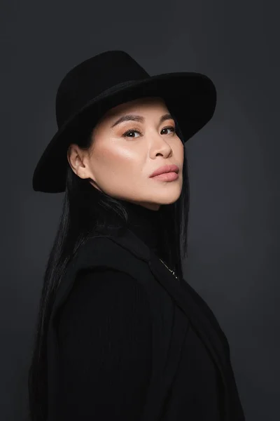 Portrait of asian model in jacket and fedora hat looking at camera isolated on dark grey — Stock Photo