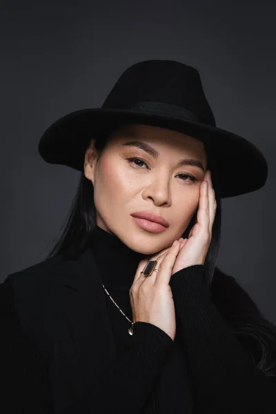 Retrato de modelo asiático em blazer e chapéu fedora olhando para câmera isolada em cinza escuro — Fotografia de Stock