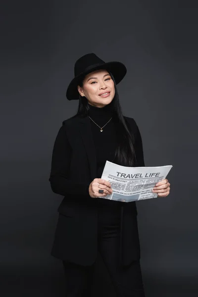 Joyeux asiatique femme en fedora chapeau et veste tenant journal isolé sur gris foncé — Photo de stock
