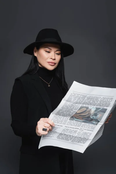 Femme asiatique en fedora chapeau et blazer lecture journal isolé sur gris foncé — Photo de stock