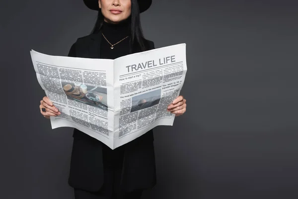 Cropped view of stylish woman in fedora hat holding travel newspaper isolated on dark grey — Stock Photo