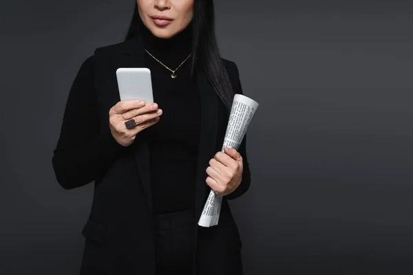 Vista recortada de mujer elegante sosteniendo periódico y teléfono inteligente aislado en gris oscuro - foto de stock