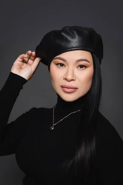 Asian model in beret and turtleneck looking at camera isolated on dark grey — Stock Photo