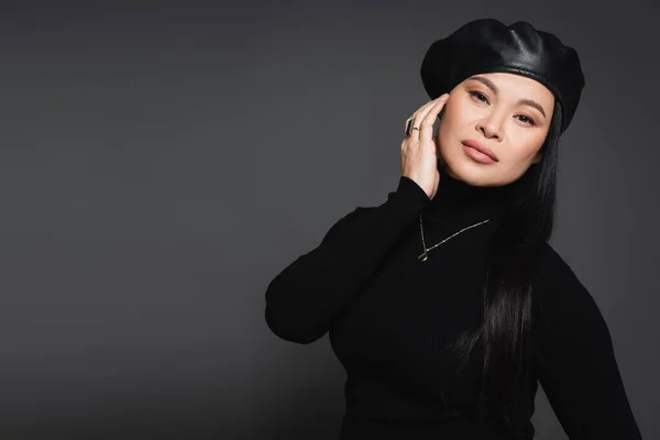 Asian model in necklace and beret looking at camera isolated on dark grey — Stock Photo