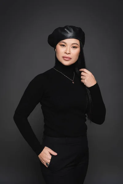 Modèle asiatique à la mode en béret tenant la main dans une poche de pantalon isolé sur gris foncé — Photo de stock