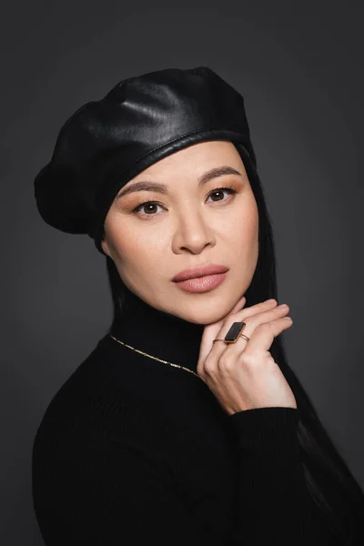 Portrait de femme asiatique en béret tenant la main près du menton isolé sur gris foncé — Photo de stock