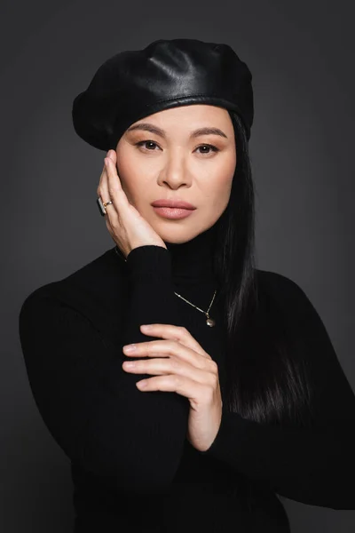 Elegantes asiatisches Model in Baskenmütze posiert und schaut vereinzelt in die Kamera auf dunkelgrau — Stockfoto