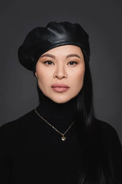 Asian model in beret and turtleneck looking at camera isolated on dark grey — Stock Photo