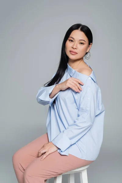 Asian woman in blouse with naked shoulder sitting on chair isolated on grey — Stock Photo