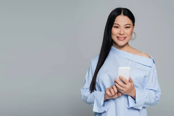 Positive asian woman in blouse using mobile phone isolated on grey — Stock Photo