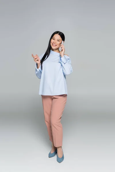 Volle Länge der stilvolle asiatische Frau sprechen auf Handy auf grauem Hintergrund — Stockfoto