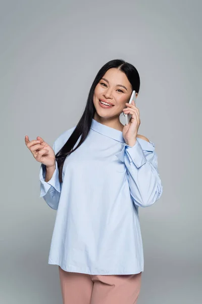 Souriant asiatique modèle en chemisier parler sur smartphone isolé sur gris — Photo de stock