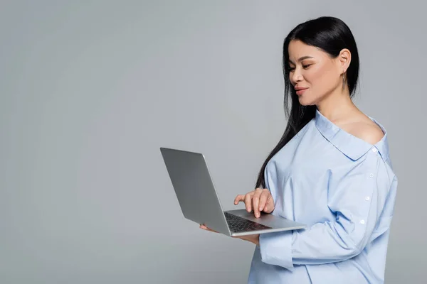 Asian woman in blouse with naked shoulder using laptop isolated on grey — Stock Photo