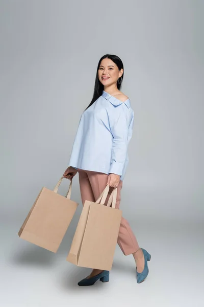 Smiling asian shopaholic holding shopping bags on grey background — Stock Photo