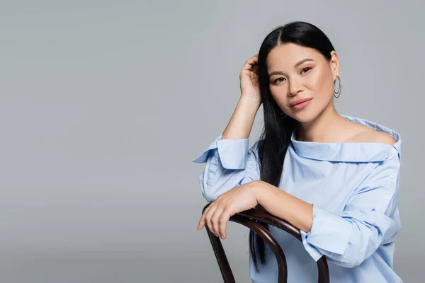 Trendy asian model looking at camera near chair isolated on grey — Stock Photo