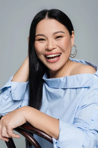 Positive asiatique femme assis sur chaise isolé sur gris — Photo de stock