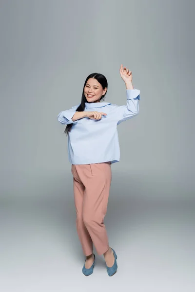 Souriant modèle asiatique en chemisier dansant sur fond gris — Photo de stock